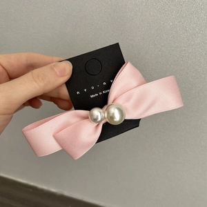Close-up of pink satin bow hair clip with faux pearl details on a black card