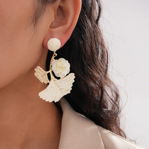 Detailed view of woven raffia flower and ginkgo leaf earrings on female model