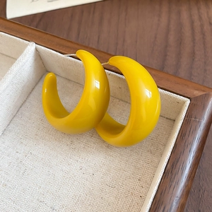 Gros plan de boucles d'oreilles créoles en résine jaune dans un coffret en lin