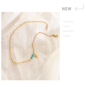 Detail of gold anklet with turquoise beads and leaf pendant on white fabric background