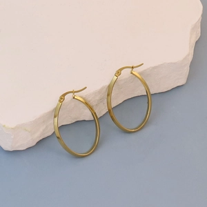Detail of gold oval hoop earrings hanging on stone against a blue background