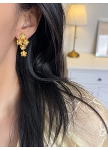 Detailed view of long gold flower earrings with white crystals on a fashion model