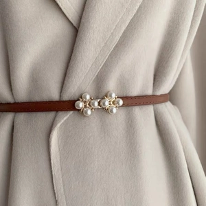 Detail of thin brown leather belt with gold pearl buckle on a beige coat outfit