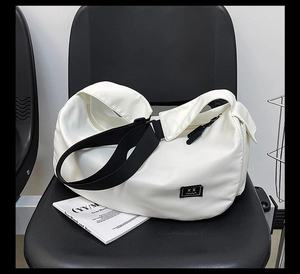 Detail of white nylon fitness bag on black chair featuring embroidery and adjustable strap