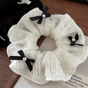 Detail of white lace scrunchie with black satin bows and elegant pearl accents