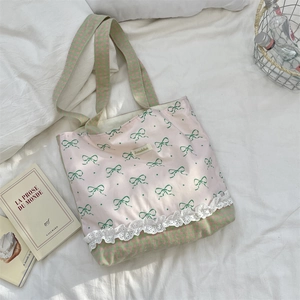 Close-up of pink canvas tote featuring lace trim and green bow print on a bed