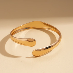 Detail shot of a polished gold oval open bangle showing smooth mirror finish and curvy lines