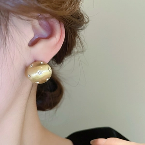Close-up of golden matte round stud earrings with shimmering inlaid crystals on model
