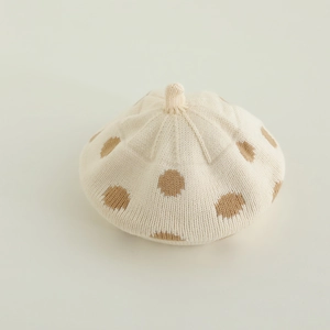 Close-up of knit beret featuring brown polka dots on a cream white wool texture