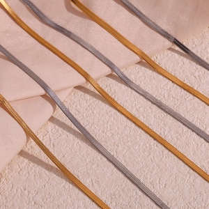 Detailed view of flat snake bone chains in gold and silver over soft silk fabric