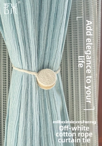 Detail of cream cotton rope curtain tieback with spiral texture on light blue drapes