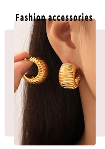 Close-up of chunky gold-plated C-shaped earrings with vertical ribbed texture on model
