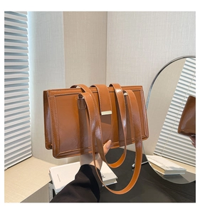 Detail of brown glossy leather handbag with metal buckle and dual handles in soft light