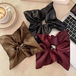 Three premium PU leather scrunchies in black, brown, and burgundy on a textured background