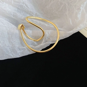 Close-up of a gold irregular twisted metal ear cuff on a white textured paper background
