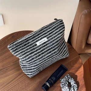 Close-up of textured black and white tweed makeup bag with simple wish label on wood table