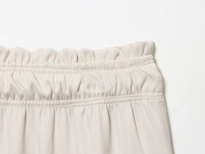 Detailed close-up of elastic waistband on off-white twill trousers with fine texture