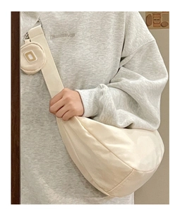 Dettaglio borsa a mezzaluna in nylon crema con tracolla larga e mini tasca rotonda