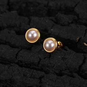 Minimalist gold-framed pearl stud earrings with secure screw backs on charcoal background