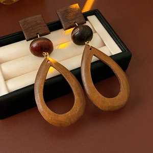 Macro detail of geometric wooden drop earrings with square and teardrop shapes on white lining
