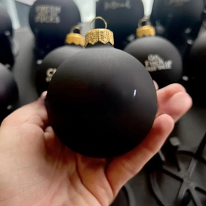 Close-up of matte black Christmas ornament with gold cap and white lettering detail