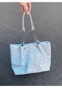 Close-up of light blue denim tote bag with silver chain handles and rivet details