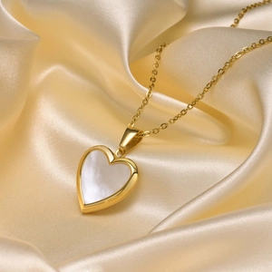 Close-up of heart-shaped gold locket with white pearl shell on champagne silk fabric