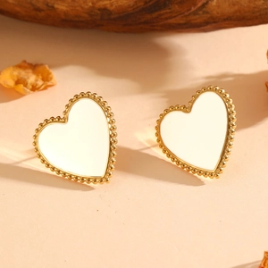 Macro detail of heart-shaped white enamel earrings with golden beaded edges on soft background