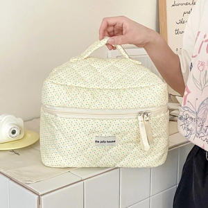 Close-up of quilted cotton cosmetic bag with polka dots, top handle, and brand label