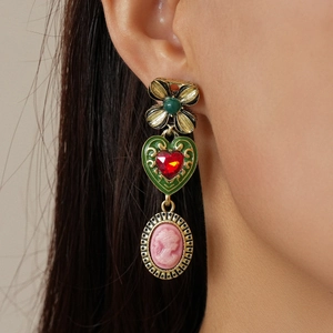 Close-up of vintage earrings featuring green heart gems and pink female portrait cameos