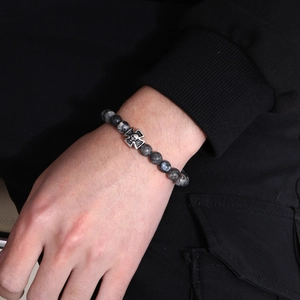Detail of beaded bracelet with tiger eye stones and a silver skull cross pendant on wrist
