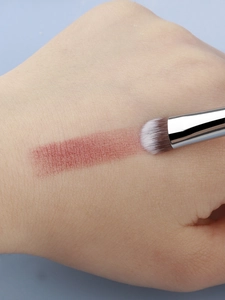 Macro shot of makeup brush applying shimmery reddish-brown powder on skin surface