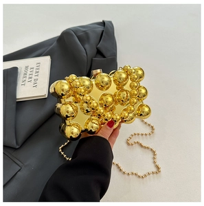 Detail of gold acrylic clutch with metallic sphere texture and chain strap being held