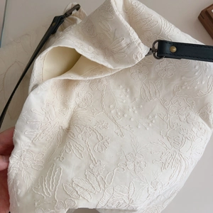 Detail showing beige tote bag with floral embroidery and black leather strap attachment