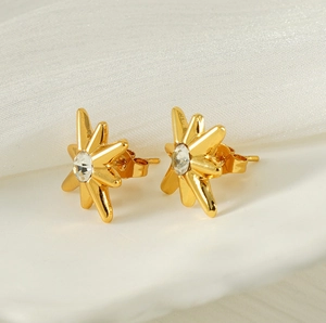 Macro view of gold starburst earrings with central zircon on white silk background
