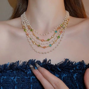 Detailed view of layered pearl and colorful gemstone necklace worn on a tweed jacket
