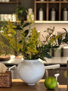 Close-up of a white ceramic vase with subtle textures and fresh yellow floral arrangement