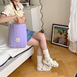 Detail of purple quilted heart tote bag with logo tag shown in cozy bedroom setting
