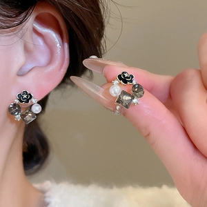 Dettaglio di orecchini a fiore con perle nere e cristalli indossati con stile