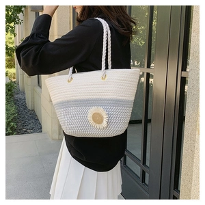 Detail of hand-woven straw tote with daisy floral accent and white rope strap
