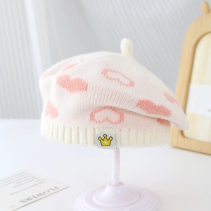 Close-up of white knit beret featuring pink heart patterns and crown tag detail