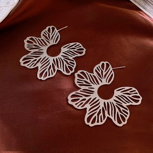Close-up of silver hollow floral earrings on a dark red silk textured background