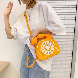 Retro orange patent leather crossbody bag in creative telephone shape worn by a model
