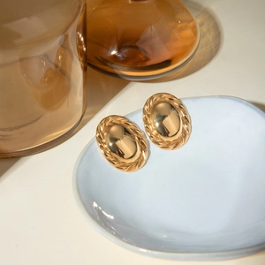 Gold stainless steel oval earrings with rope border and smooth center in a ceramic dish
