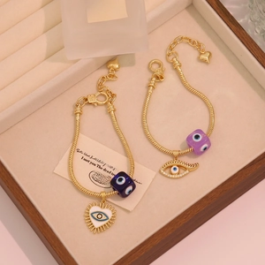 Golden Evil Eye snake chain bracelets with heart and bead charms in a wooden tray