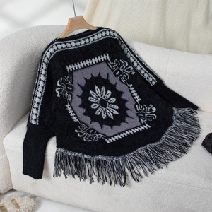 Detail of black knit poncho featuring grey geometric floral patterns and fringe hem