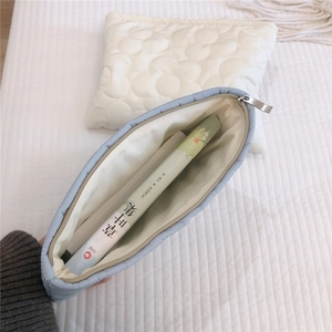 Close-up of light blue quilted pouch with smooth metal zipper and spacious beige lining