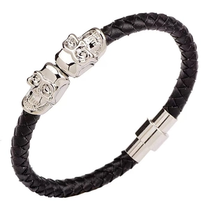 Detailed close-up of men's black braided leather bracelet with silver skull charms and magnetic clasp