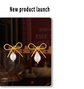 Macro shot of gold bow stud earrings with white teardrop pearls on a wooden display