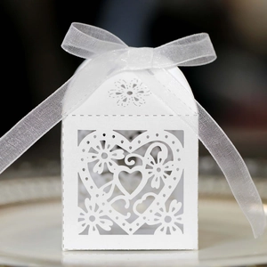 Detailed laser-cut heart and floral patterns on white wedding favor box with ribbon